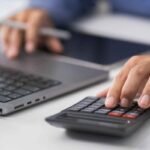 Mãos usando calculadora e laptop para contabilidade automática